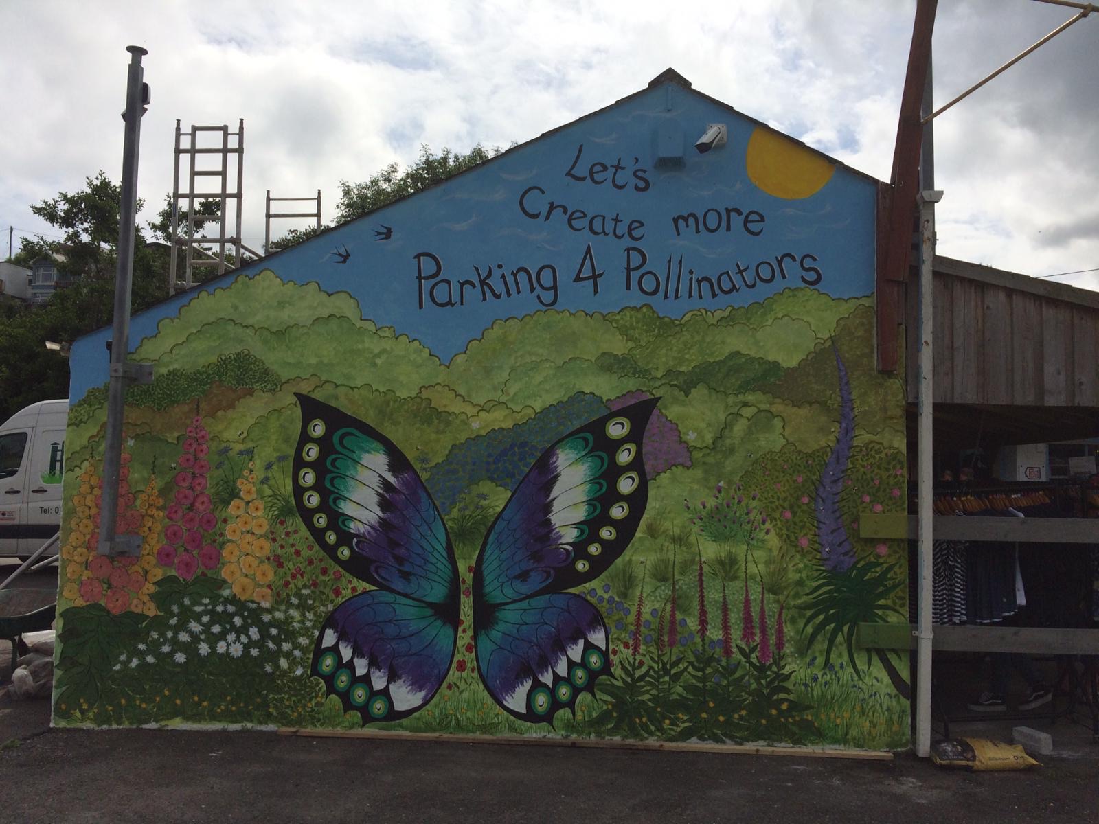 A painted mural of a butterfly and wildflowers on a gable end, reading &ldquo;Let&rsquo;s create more parking 4 pollinators&rdquo;